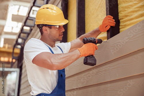 Male builder using power drill at construction site