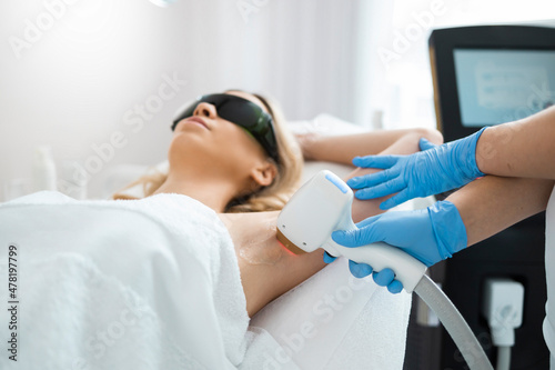 Woman on underarm laser epilation procedure in beauty clinic. Beautician removing hair of pretty blonde armpit