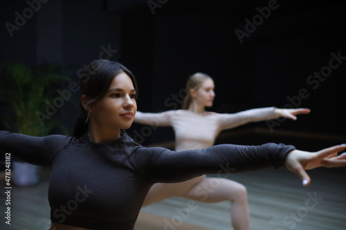 Two sportive women practicing doing yoga in the studio spreads their hands in different directions