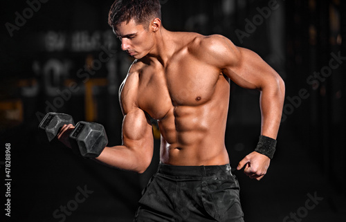 Bodybuilding concept. Brutal strong muscular bodybuilder athletic man pumping up muscles with barbell on black background. Workout bodybuilding concept. Copy space for sport nutrition ads.