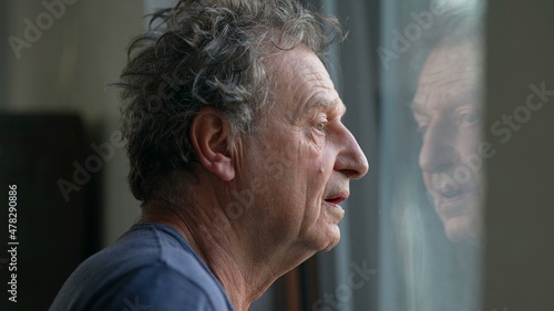 Pensive senior man standing by window looking outside. Thoughtful old person