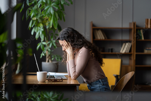 Young frustrated female employee getting stuck on task or project, sitting in front of laptop holding head in hands and thinking, tired account manager cant deal with deadline at work. Selective focus