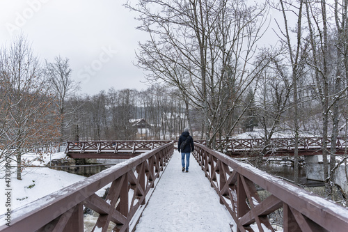 A man crosses the river in winter on a wooden bridge