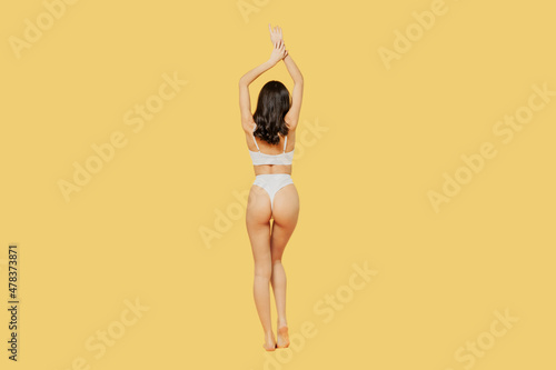 Full body back view confident beautiful young sexy brunette woman 20s in white underwear with perfect fit figure raise up hands isolated on plain yellow background studio People female beauty concept