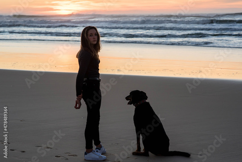 beautiful young woman with long hair walking on the beach in the evening with her dog