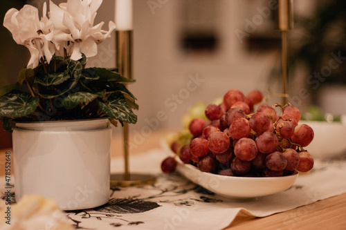 Red grapes on a white plate on a decorated holiday table next to a flower in a pot.