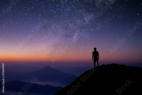 Silhouette of young man standing and watched the star, milky way and night sky alone on top of the mountain. He enjoyed traveling and was successful when he reached the summit.