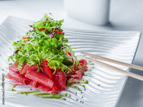 Elegant salad with veal carpaccio in a white bowl with chopsticks.