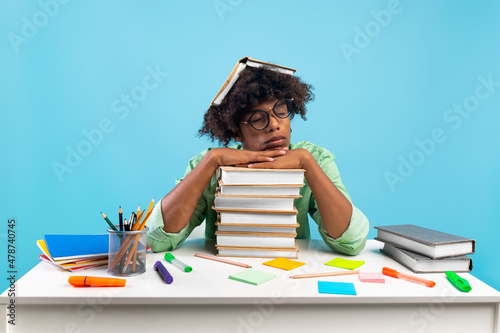 Tired african american student guy having nap on books, being exhausted during preparing for exams, blue background