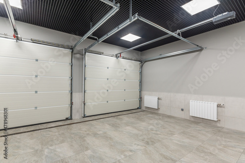 Modern garage for two places with automatic gates, with gray granite floor tiles and light walls.