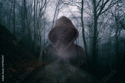 A horror concept of a double exposure of a scary hooded figure with no face. In a moody, foggy forest on a winters evening