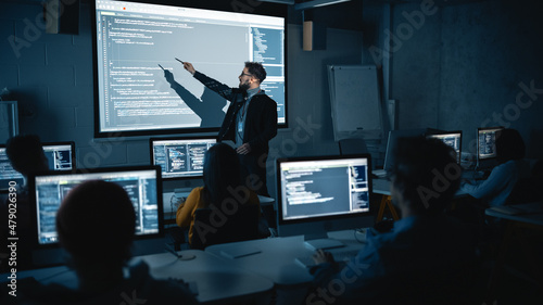 Teacher Giving Computer Science Lecture to Diverse Multiethnic Group of Female and Male Students in Dark College Room. Projecting Slideshow with Programming Code. Explaining Information Technology.