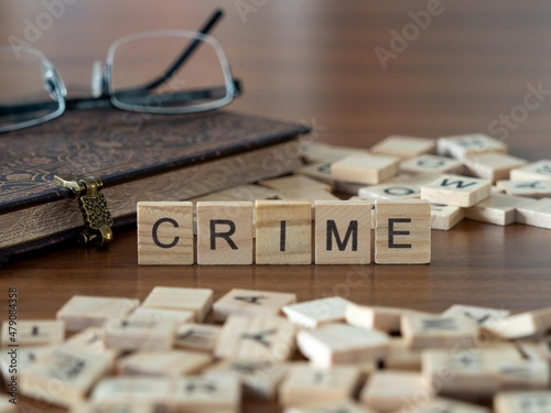 crime concept represented by wooden letter tiles on a wooden table with glasses and a book