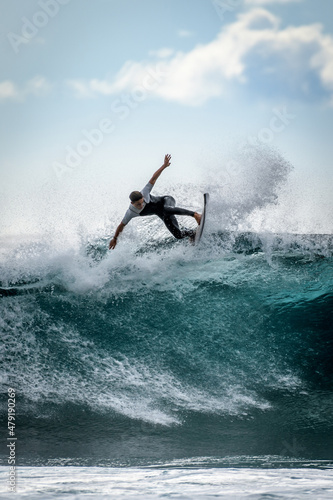 Young surfer with with wetsuit enjoying big waves in Tenerife, Canary Islands. Sporty boy riding his surf board on the ocean wave. Brave teenager making tricks on the rough sea during a competition.