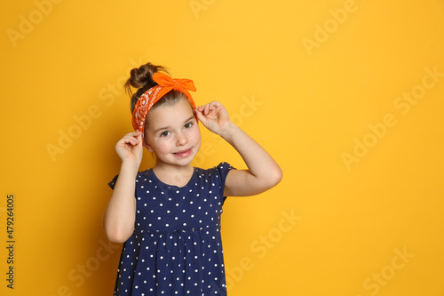 Cute little girl wearing stylish bandana on orange background, space for text