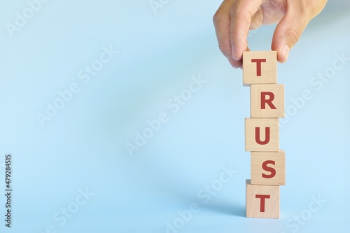 Build trust concept. Hand stacking wooden blocks with word trust.