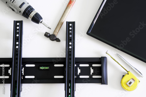 TV wall mount bracket, electric drill, fountain pen, tape measure, hammer and monitor on a white background. The concept of mounting a TV or computer monitor on a wall