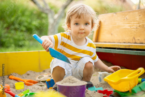 A little boy playing in the sandbox at the playground outdoors. Toddler playing with sand molds and making mudpies. Outdoor creative activities for kids