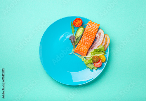 Intermittent fasting low carb hight fats diet concept flat lay, healthy food salmon fish, bacon meat, vegetables and salad on blue plate and blue background top view 