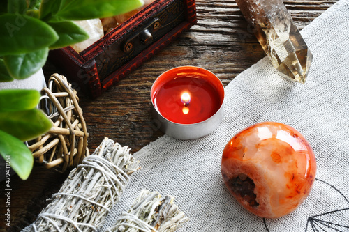 A close up image of a red carnelian crystal with a lit red candle and Smokey quartz tower on a sacred geometry grid cloth. 