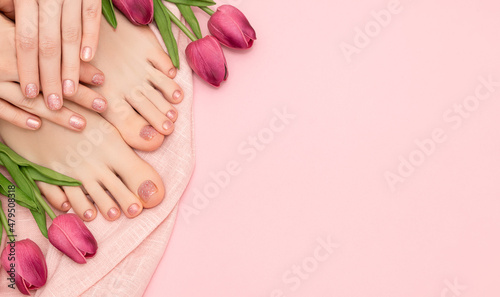 Female hands with spring nail design. Glitter pink nail polish pedicure. Female hands and feet with tulip flowers on pink background. Copy space.