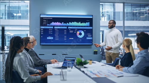 Office Conference Room Meeting Presentation: Black Businessman Talks, Uses TV Screen to Show Company Growth with Big Data Analysis, Graphs, Charts, Infographics. e-Commerce e-Business.