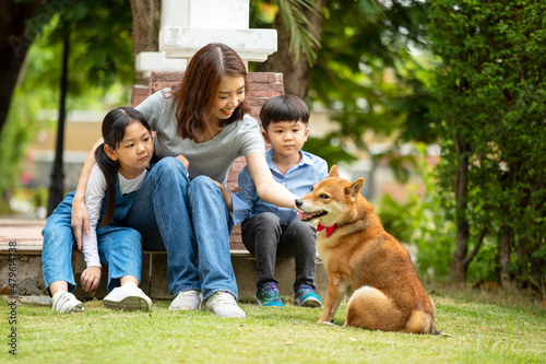 Asian mother and two kids sitting and playing together with Shiba inu dog in public park