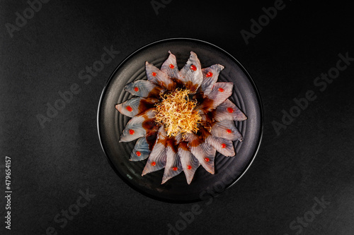 Fish carpaccio in a black plate with sweet potato straws.