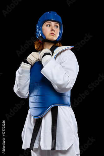 Portrait of young girl, taekwondo practitioner posing isolated over dark background. Concept of sport, skills