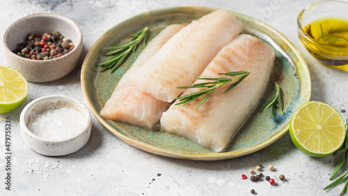 Raw fresh cod loin fillet steak with aromatic herbs, spices, lime and olive oil on gray background. Healthy food and diet concept. banner