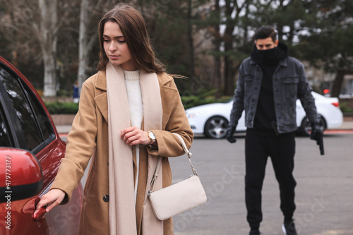 Man with gun stalking young woman on parking lot outdoors