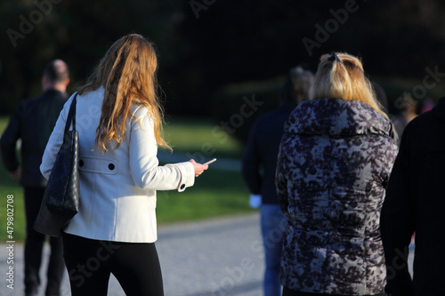 Kobieta z telefonem w ręku spaceruje w parku z koleżanką.