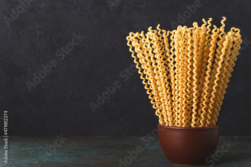 Raw fusilli bucati pasta in bowl on dark background with copy space