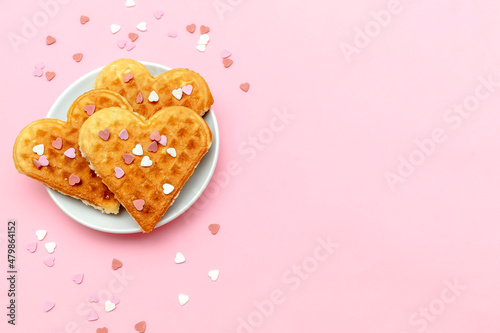 Homemade Belgian waffles heart shaped on plate with colorful sweet mini confetti, sprinkles food. pink background for Valentines day, womens day, love, romance, party pattern with copy space
