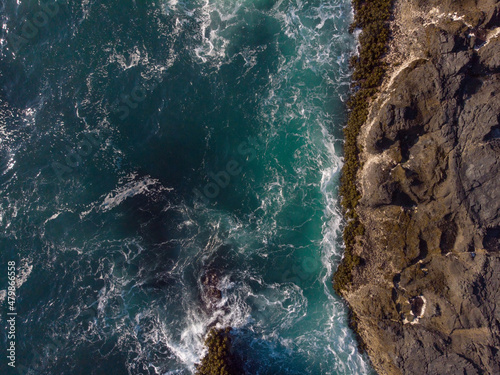 Aerial photograph. Seething ocean water. Foam waves crash against the rocky shore. Beautiful nature. Ecology, geology. Color image. There are no people in the photo. Minimalism. Abstraction.