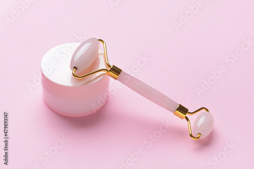 Face massage roller with cosmetic cream on color background
