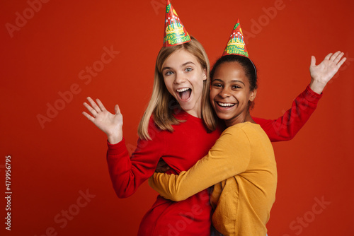 Multiracial girls wearing party cones laughing while hugging together