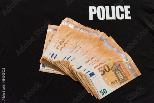 Une liasse de billets de 50 euros sur un t-shirt noir de police - format paysage