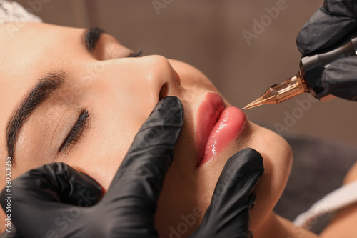 Young woman undergoing procedure of permanent lip makeup in tattoo salon, closeup