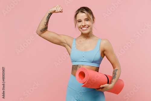 Young strong sporty athletic fitness trainer instructor woman wear blue tracksuit spend time in home gym show hand biceps muscles isolated on pastel plain light pink background. Workout sport concept.