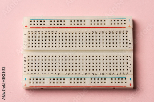An electronics breadboard on pink background..