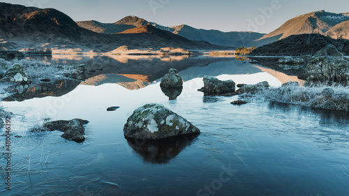 Ice on the shore of a lake with reflecting peaks.