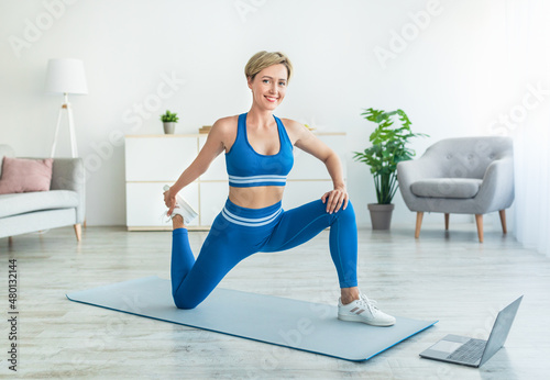 Cheerful woman stretching leg muscles using laptop pc