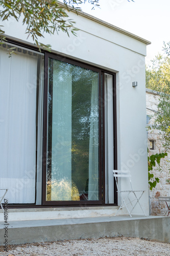 Glimpses of a renovated and refurbished typical stone house in Apulia region of Italy, called LAMIA, a minimal, square stone and concrete house. Detail of bedroom door window with white curtains.