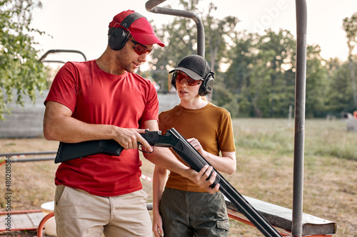 handsome caucasian man and young woman checking details of weapon before training loading gun outdoors, sport shooting. trainer and female going to practice shooting together in polygon