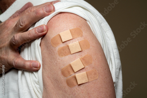Senior caucasian man sleeve to show the fourth booster coronavirus vaccine shot in the shoulder. Concept with four separate bandages for the shots