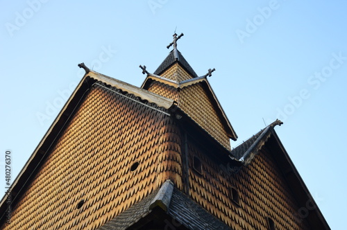 Medieval wooden stave church in Heddal, Norway. Carved wooden dragon heads, wooden shingle, wooden cross on the top of the tower, blue sky