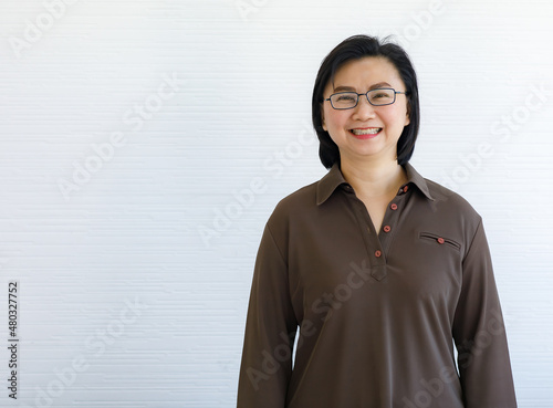 Portrait closeup studio shot of Asian happy middle aged short hair female businesswoman model in casual outfit and eyeglasses standing crossed arms smiling look at camera on white wall background