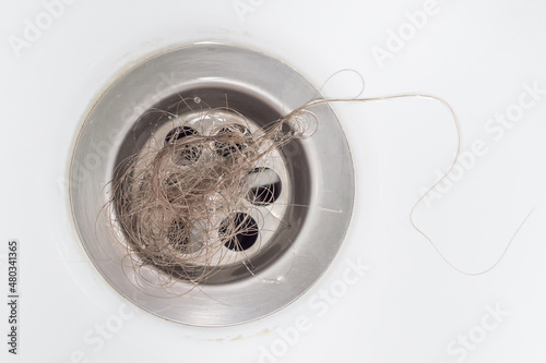 A bundle of blonde women's hair was left in the bathroom drain after taking a shower. Close-up, top view. The problem of hair loss.