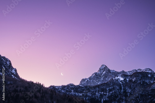 Crescent waning moon in purple sky overy mountain peaks